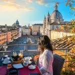 Een vrouw geniet van het uitzicht op Rome, Italië en het Piazza Navona terwijl ze haar continentale ontbijt afmaakt vanaf een dakterras van een luxe hotel op een vroege zomerochtend.