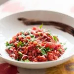 Nahaufnahme eines italienischen roten Gourmet-Risottos mit Rüben, Petersilie, Käse und Balsamico-Essig aus Modena in einem weißen Teller auf einem Tisch mit Tuch