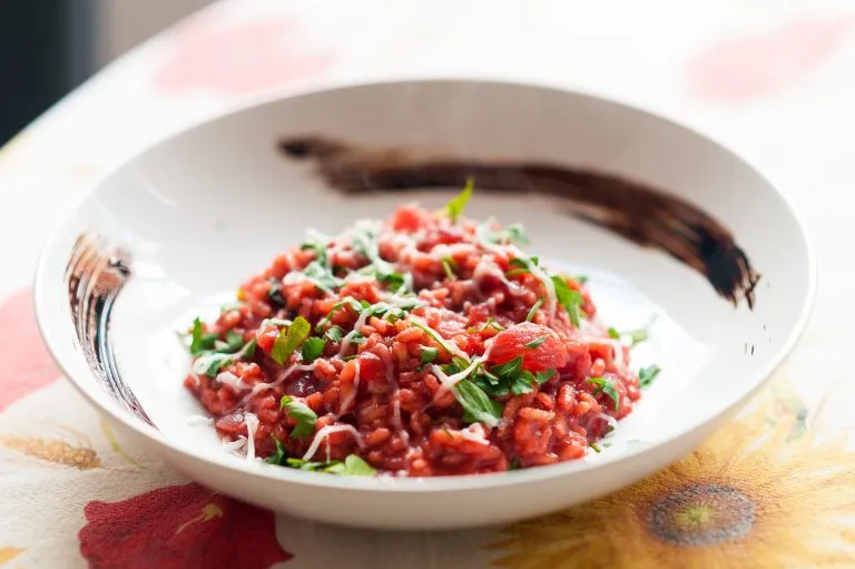 close up of italian red gourmet risotto dish with beet, parsley, cheese and modena balsamic vinegar in white plate on table with cloth