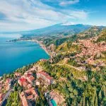 View from flying drone. Sunny morning view of Taormina town and Etna volcano on background. Nice spring seascape of Mediterranean sea. Splendid view of Sicily, Itale, Europe.